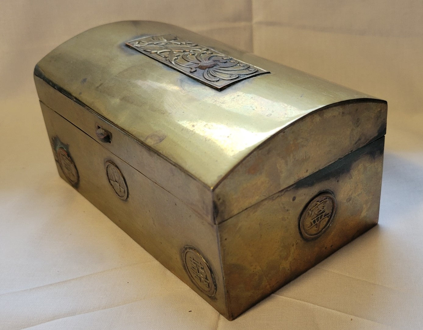 Antique brass box curio made in China, with a domed lid. The interior bottom has wood inserts on three side (one side is missing). The exterior has welded medallions with Chinese characters and designs. View of opposite corner.