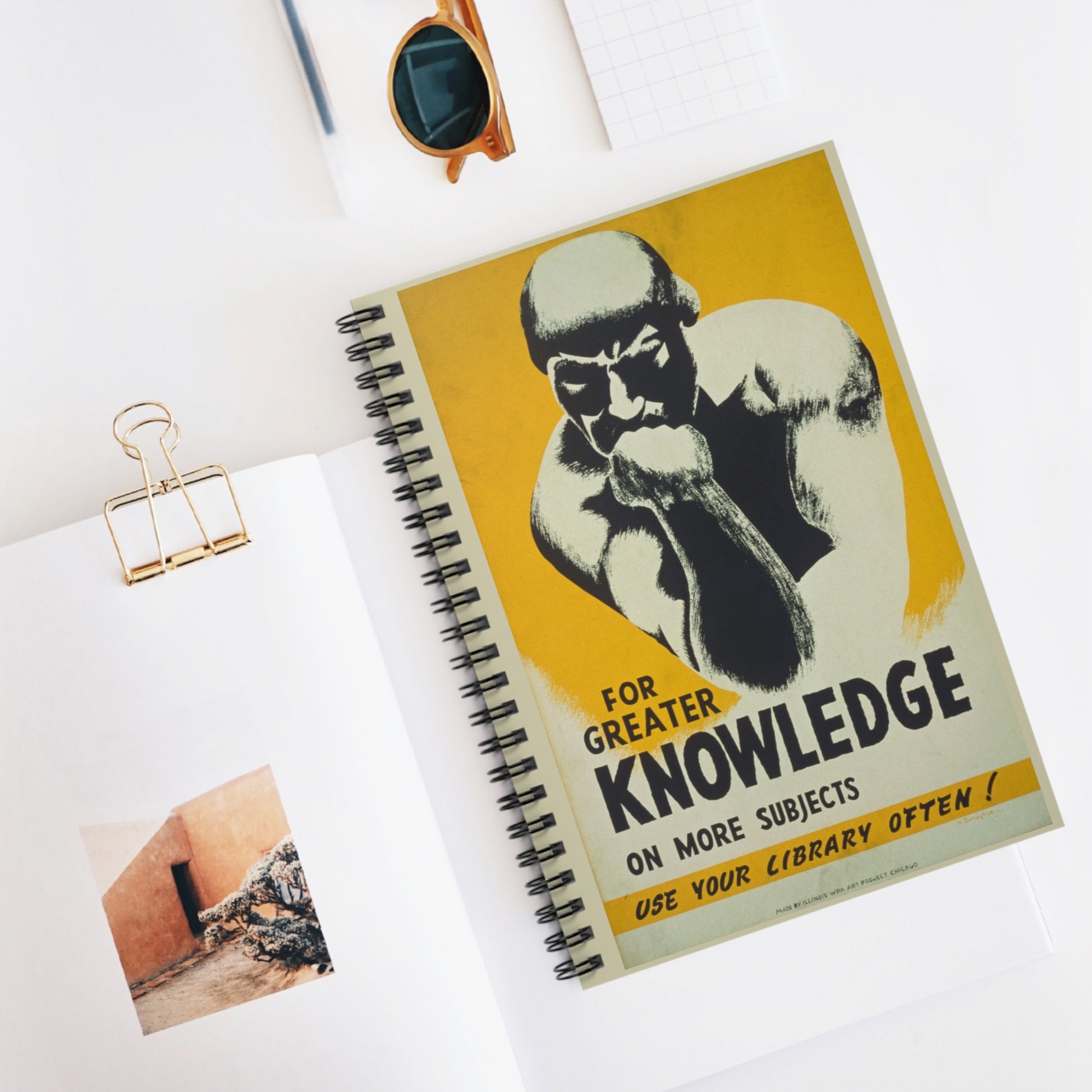 Spiral notebook, front cover is vintage poster with a yellow background and a black and white image of "The Thinker" and has the text "For greater knowledge on more subjects, use your library often!"