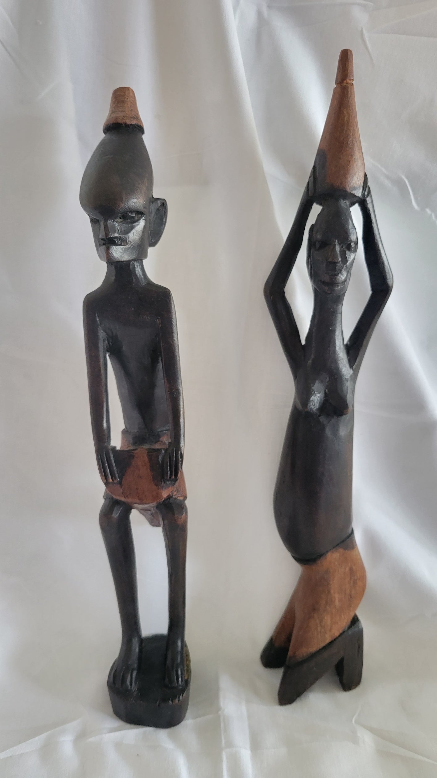 Set of two vintage wooden figures, male holding drum between knees, women with basket on head. Front view.