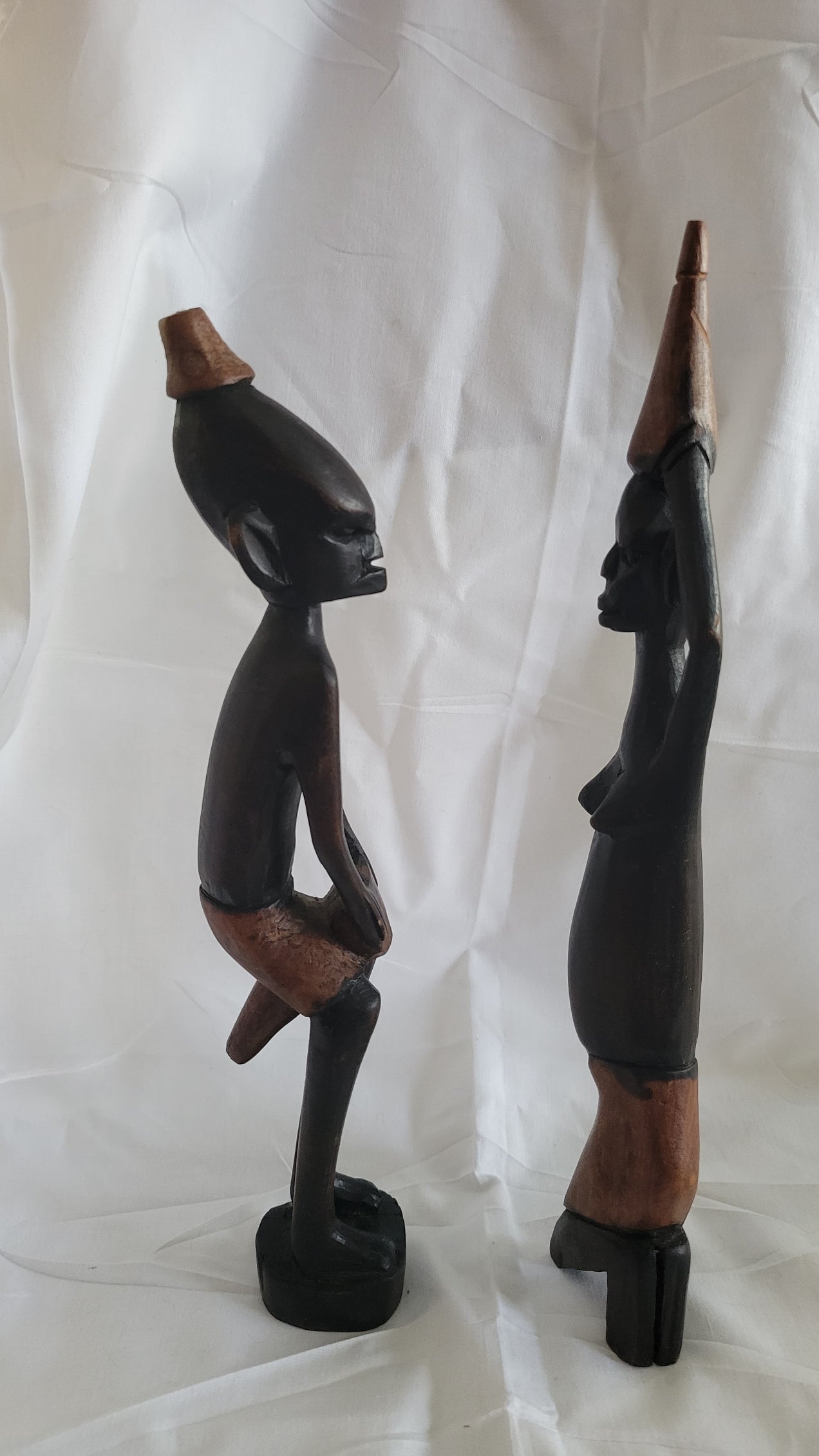 Set of two vintage wooden figures, male holding drum between knees, women with basket on head. Side view.