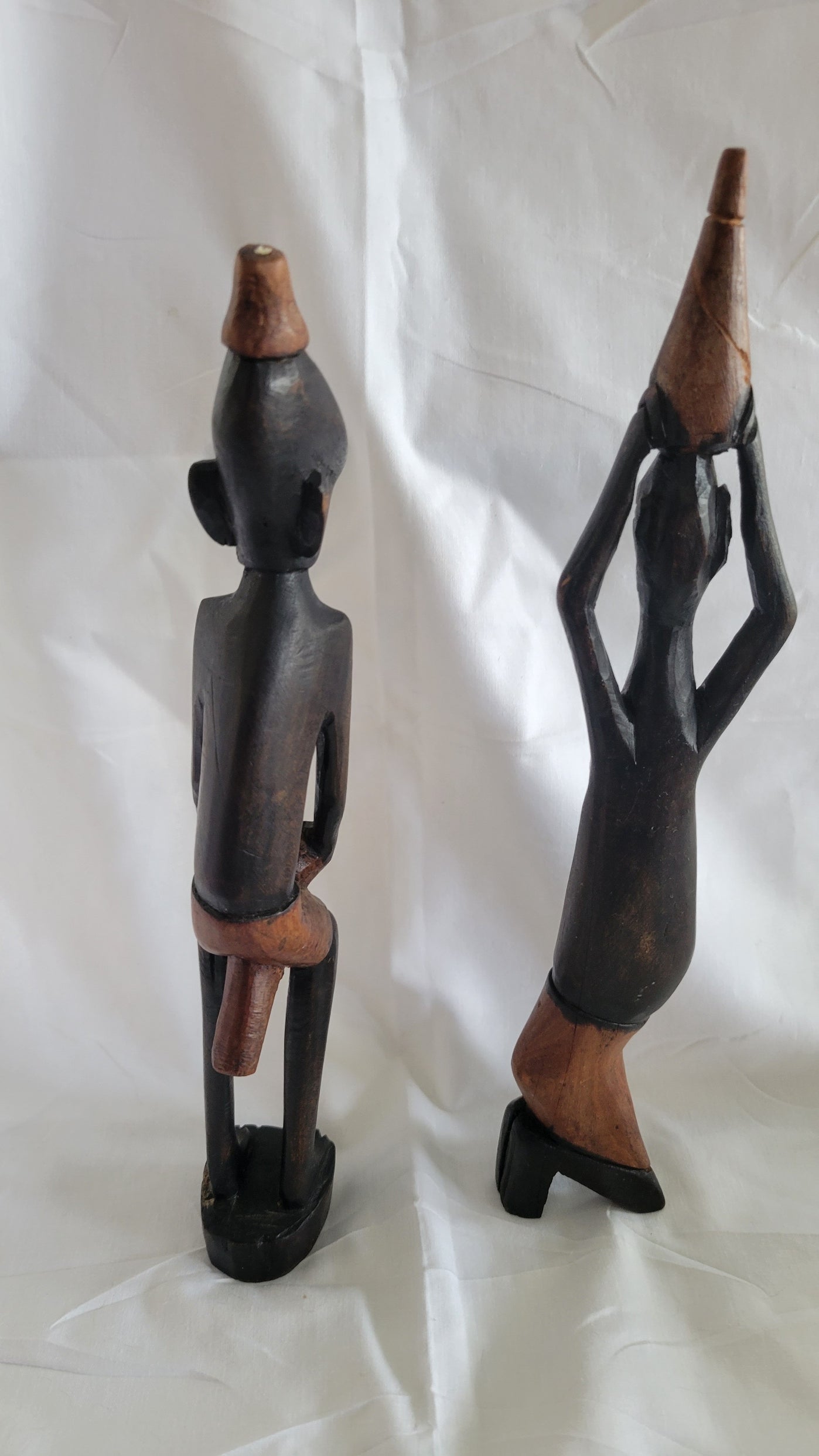 Set of two vintage wooden figures, male holding drum between knees, women with basket on head. Back view.