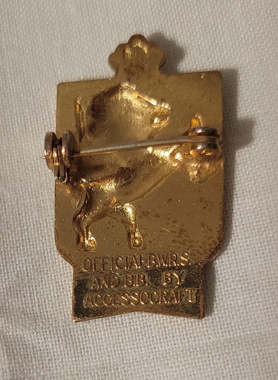 Vintage curio pin with gold lion on white background and French flag colorsbelow. "Dieu et Mon Droit" is French for "God and my right" and it is the motto of the British monarchy. Produced by Accessocraft as a fundraiser for the British war effort during World War II.  View of back, with words "Official B.W.R.S. and B.B. By Accessocraft"