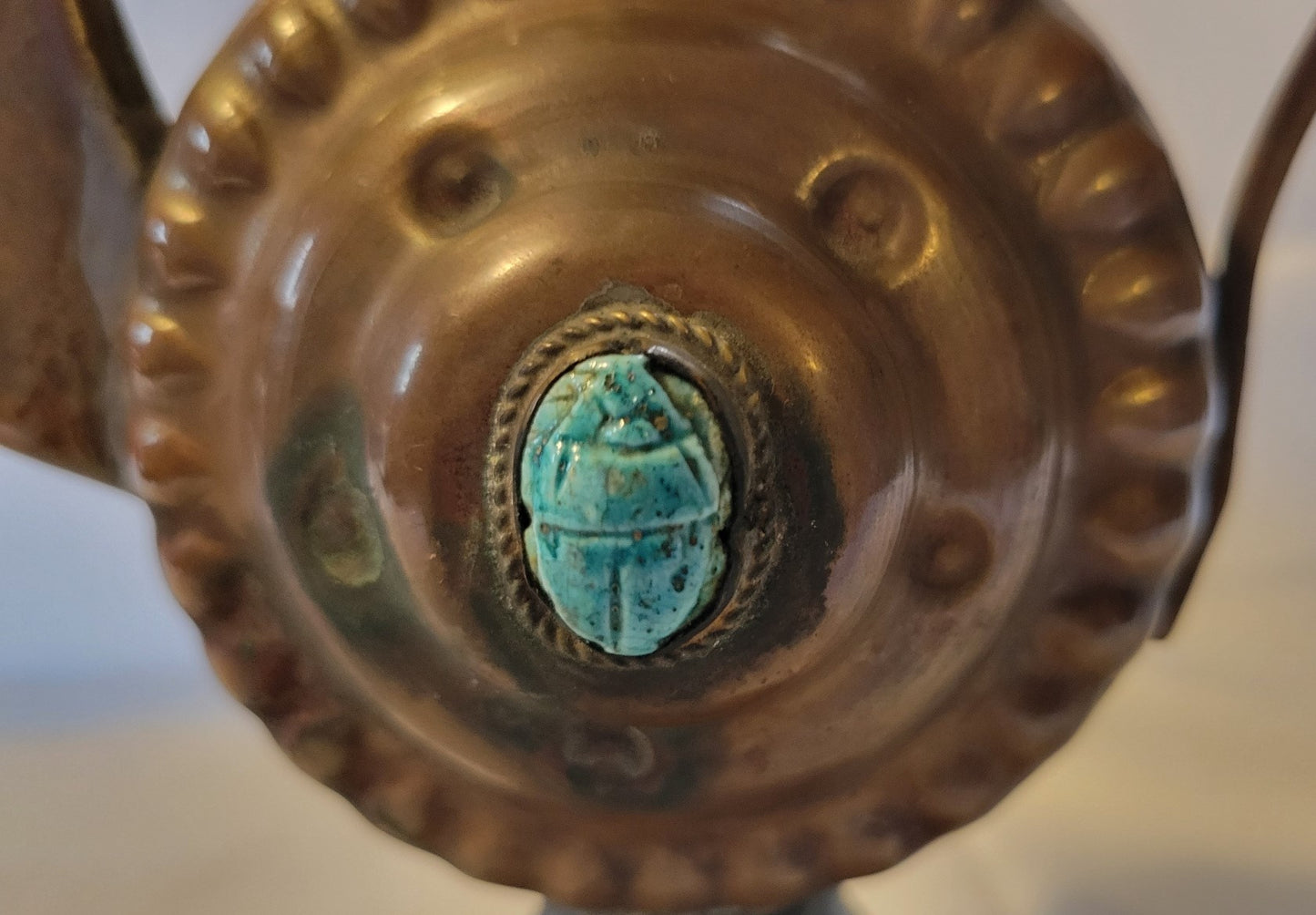 Antique, Egyptian copper kettle with a glazed turquoise scarab beetle on both sides.  The scarab beetle was a symbol of death and rebirth in ancient Egypt. Close-up view of scarab beetle.