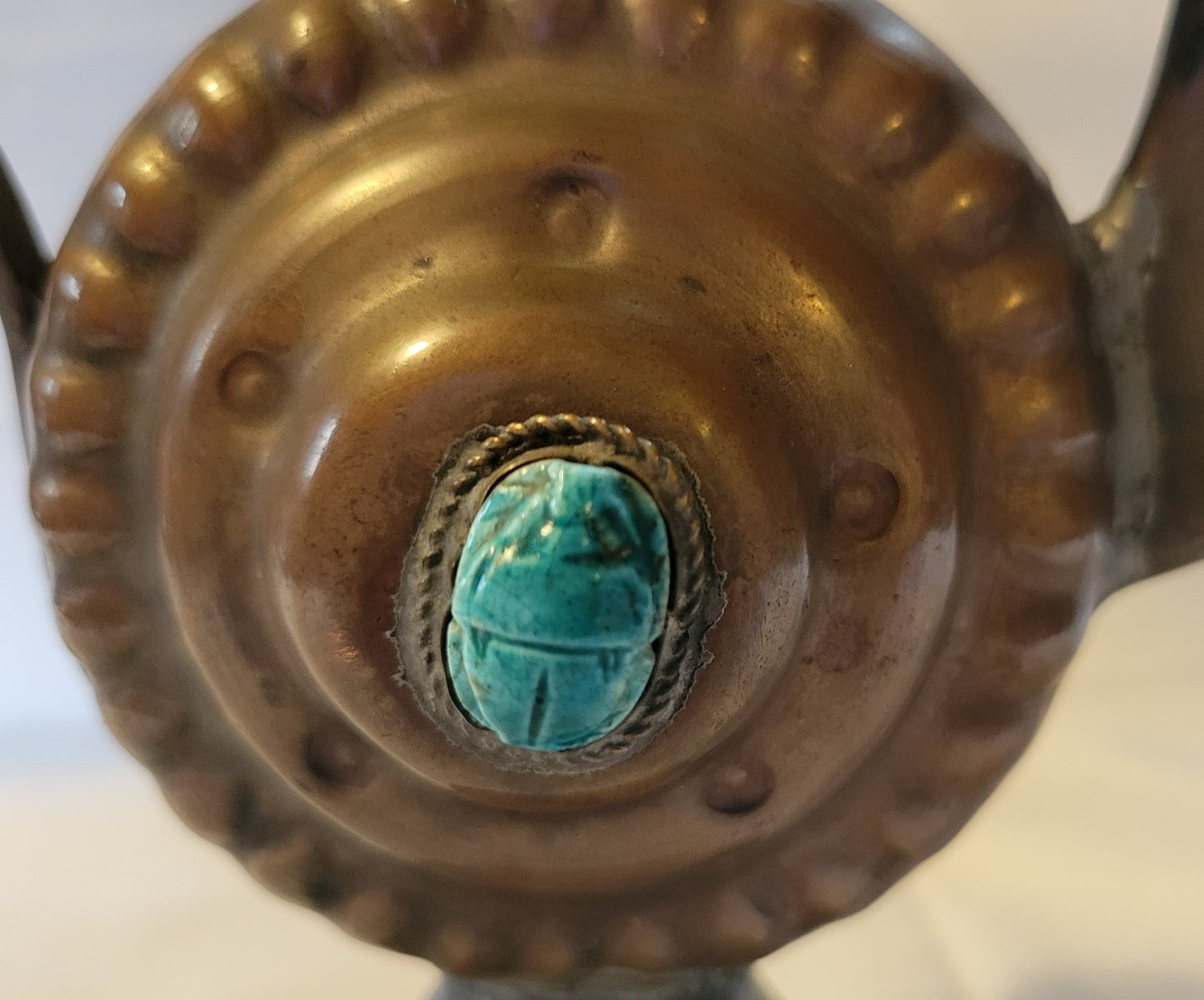 Antique, Egyptian copper kettle with a glazed turquoise scarab beetle on both sides.  The scarab beetle was a symbol of death and rebirth in ancient Egypt. Close-up view of the back scarab beetle.