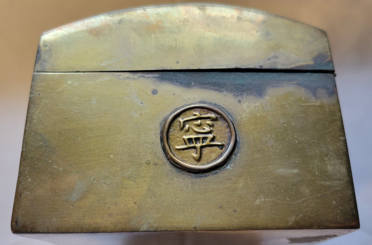 Antique brass box curio made in China, with a domed lid. The interior bottom has wood inserts on three side (one side is missing). The exterior has welded medallions with Chinese characters and designs. View of side.