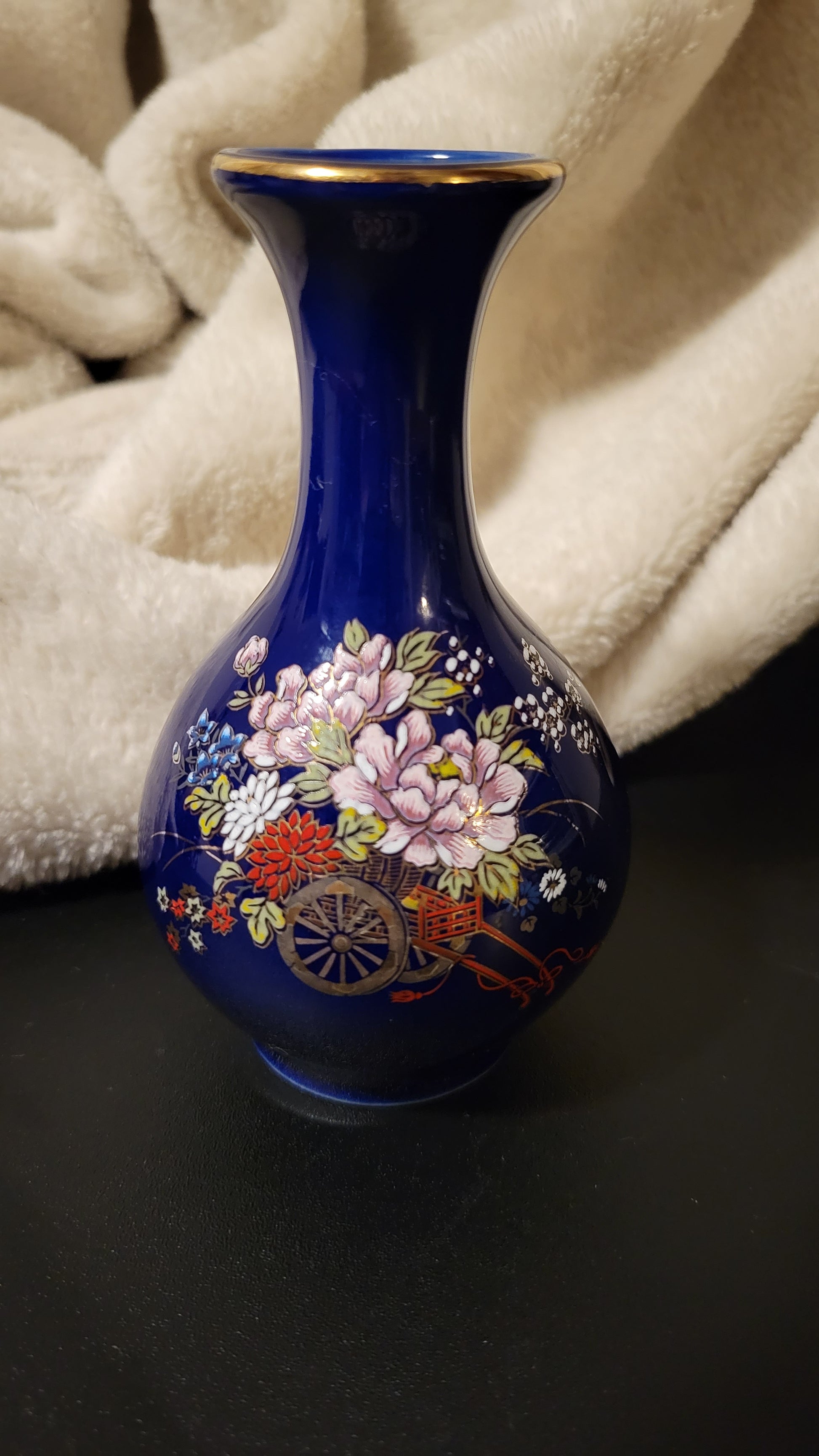 A small beautiful oriental vase, blue glass with painted flowers and a cart, with gold trim, front view.